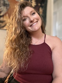 a woman in a burgundy top and black pants smiling